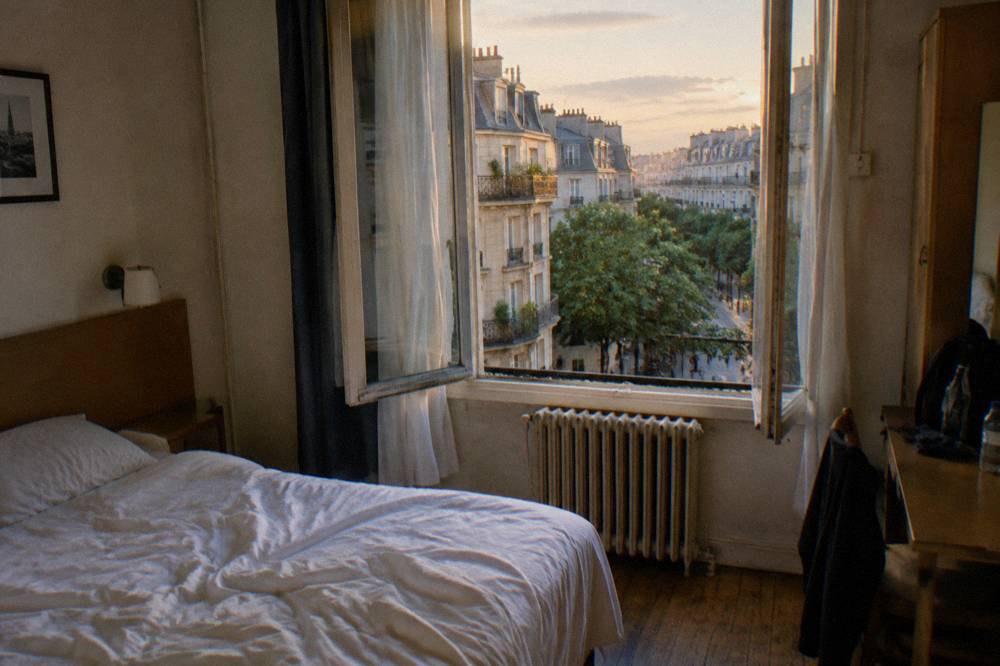 A small budget hotel room with a double bed and a window onto a Paris street