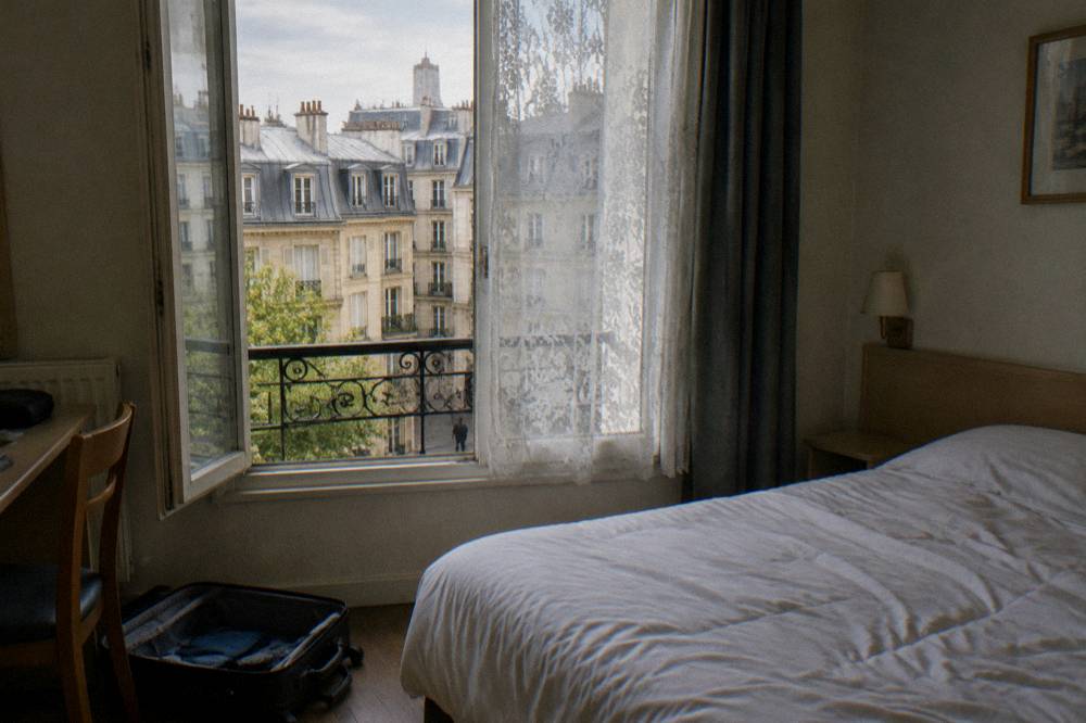 A bright budget hotel room with a double bed and a window onto a Paris street